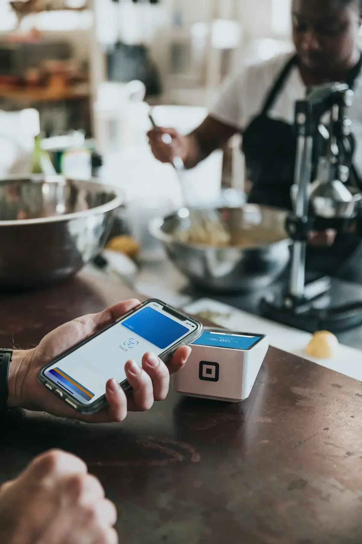 A customer paying with a phone at a card reader on a shop counter
