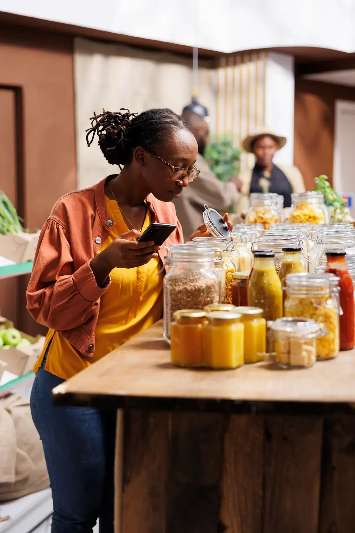 A shop owner checking her phone at a counter lined with jars of goods