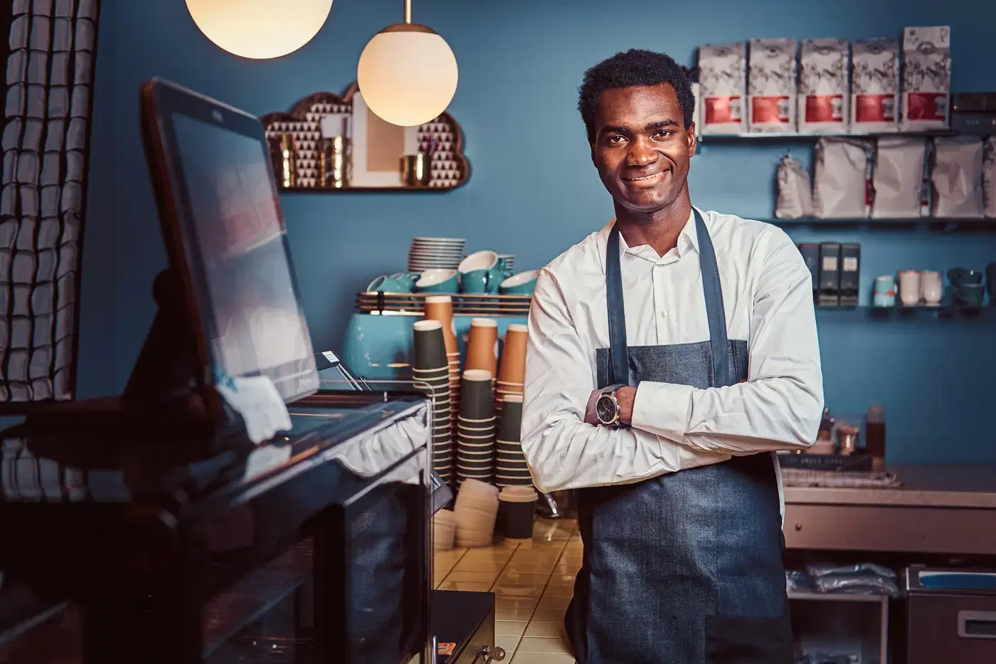 A smiling café owner in an apron standing in his coffee shop