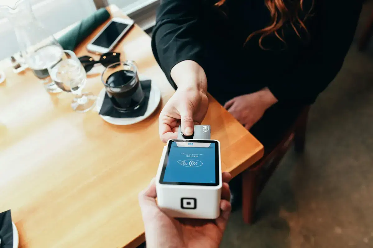 A customer tapping a card on a payment terminal at a café table