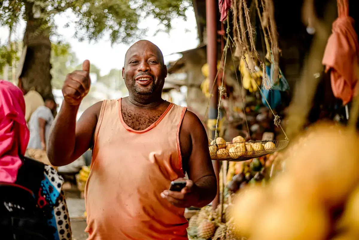 A smiling market vendor giving a thumbs up beside his stall